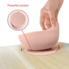 A hand lifts a pink bowl with strong suction from a wooden surface.