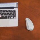 Open laptop and white mouse on a wooden desk.
