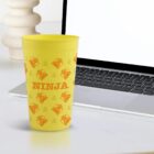 Yellow cup with NINJA and orange logos beside a laptop on a white desk.