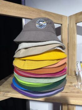 Stack of colorful bucket hats on a wooden shelf, topped with a grey APPA 2025 Space Explorer hat.