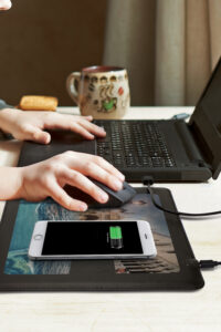 A person using a laptop with the phone charging in the wireless mouse pad