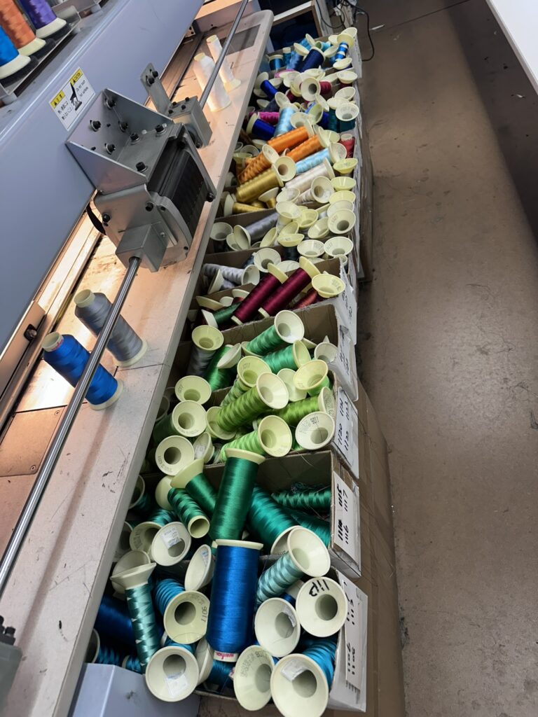 Spools of colorful thread scattered as artisans embroider logos in an Australian workspace.