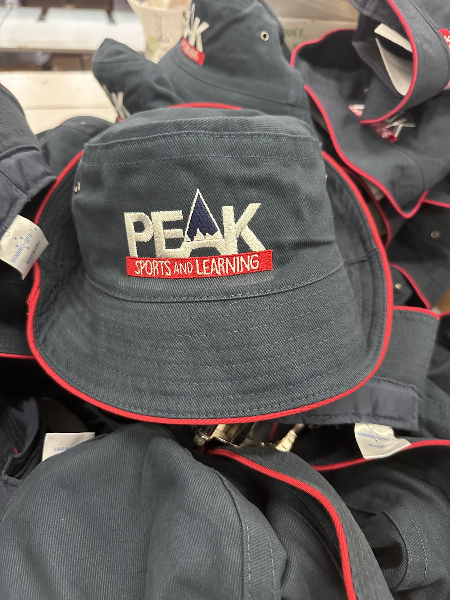 A dark bucket hat with embroider logos and PEAK Sports and Learning on the front.
