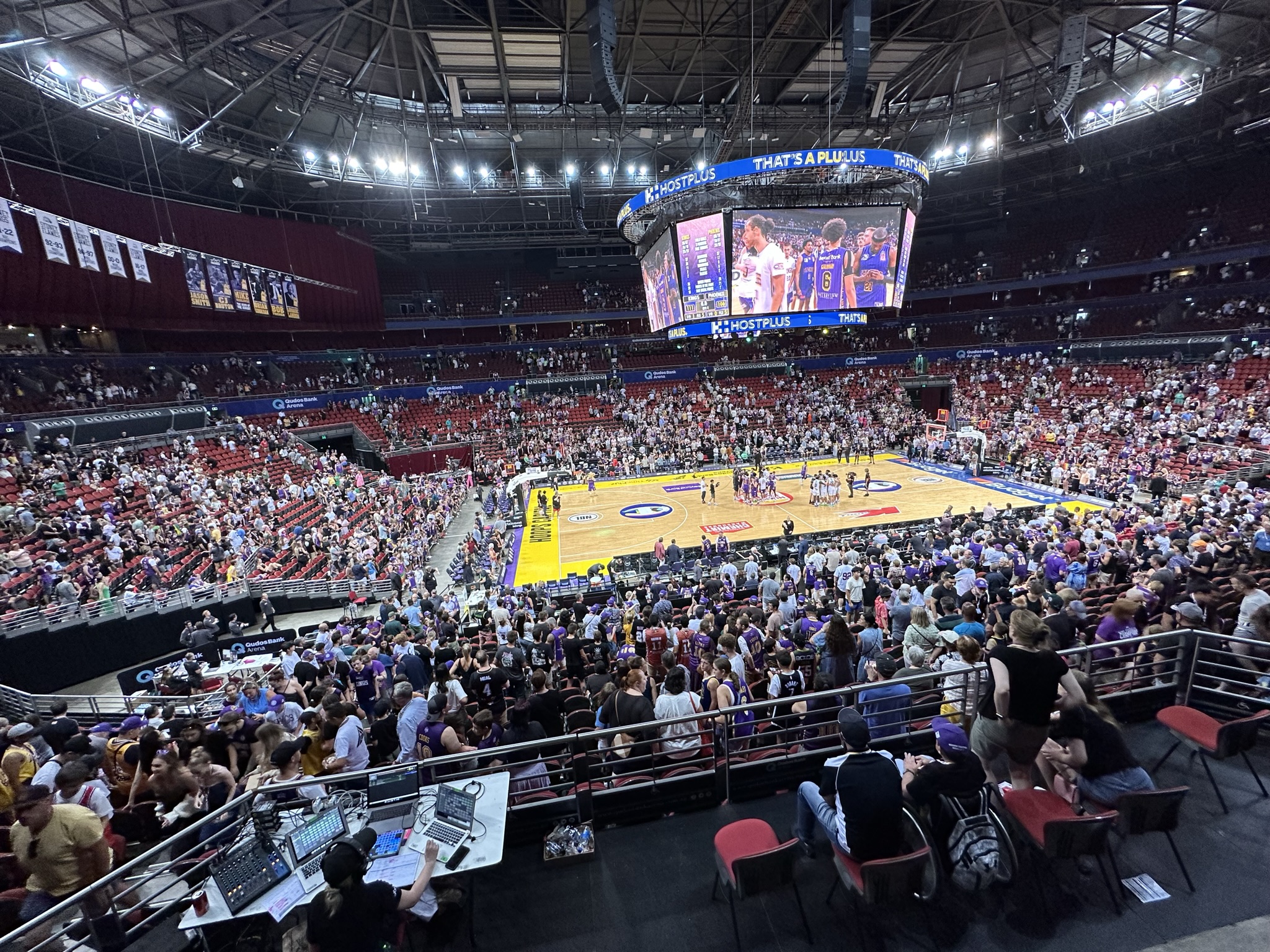 Stadium crowds fill the arena, watching the game under a scoreboard with custom-branded event gear.