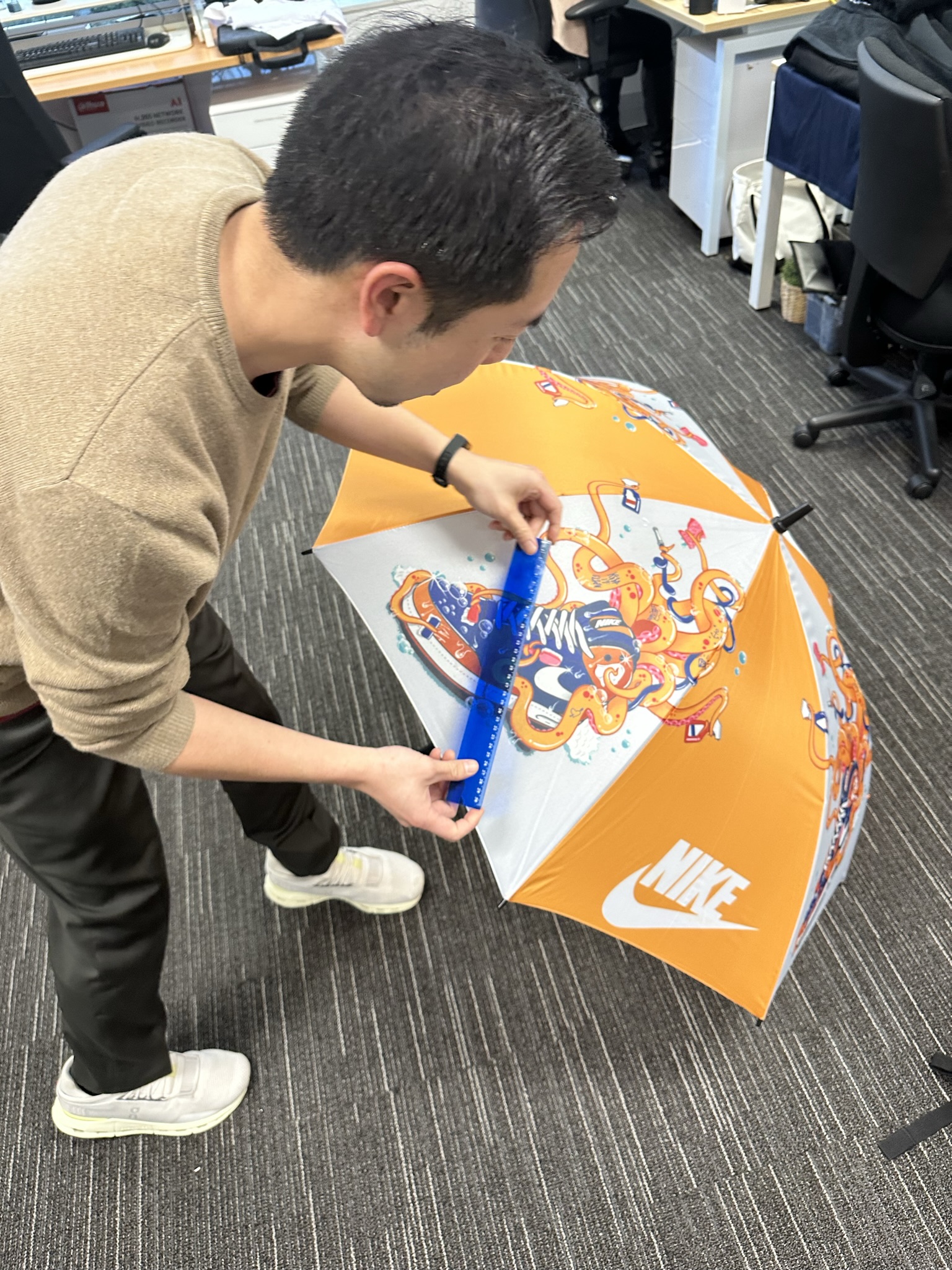Person measuring an orange Nike umbrella for product sourcing in an office with a blue ruler.