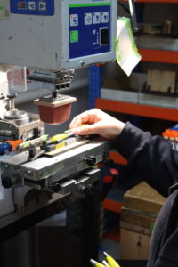 Person operating a pad printing machine, adjusting a tool on a workspace.