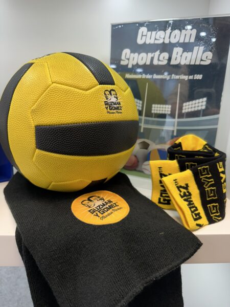 Yellow and black volleyball with top brands merch beanie and scarf on a shelf, sign in background.