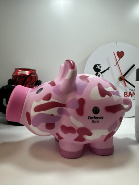 A pink camouflage piggy bank inspires merch beside a Banksy-themed clock from top brands.