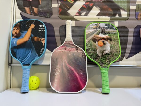 Three Pickleball Craze 2025 paddles and a yellow ball displayed on a white surface.