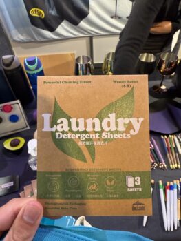A hand holds a packet of eco-friendly laundry detergent sheets at the APPA 2025 display table.