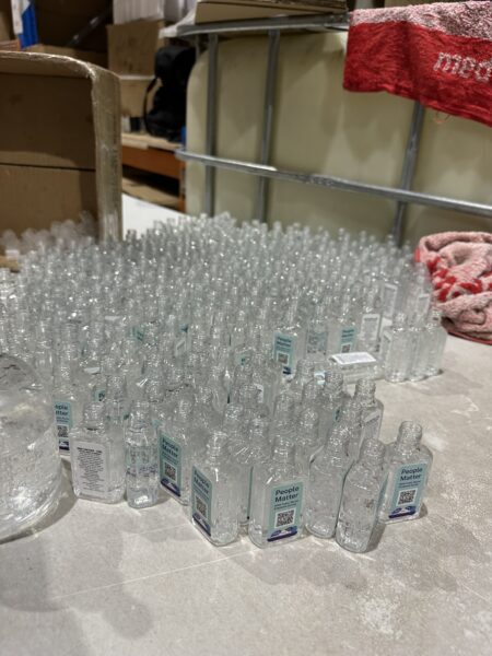 Rows of custom branded hand sanitiser bottles labeled People Matter, with boxes and towels nearby.