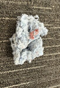 A clump of recycled lint threads on a textured carpet.