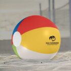 Colorful beach ball with Eau Summer logo on sandy beach near a net.