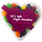 Heart-shaped box with colorful candies and lets talk organ donation on a purple label.