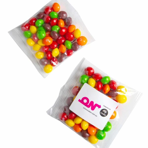 Two clear packets of colorful Skittles, one with a custom logo sticker on the front.