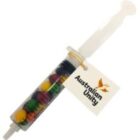 A syringe-shaped container filled with colorful candies and an Australian Unity tag attached.