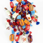 Assorted wrapped candies in various colors scattered on a white background.