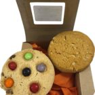 Open box with two cookies, one plain and one topped with colorful candy-coated chocolates.