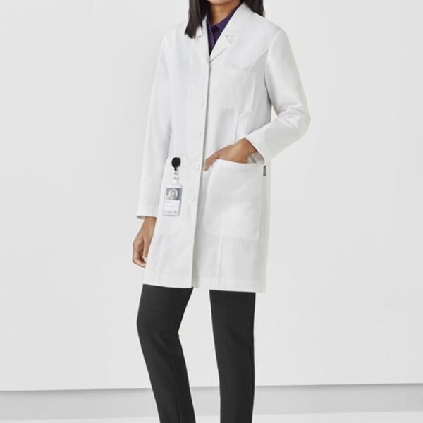 Person in a white lab coat and black pants, smiling and standing against a plain background.
