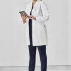 A person in a lab coat holding a tablet, smiling in a clean, white environment.