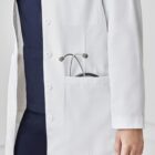 Person in white lab coat with stethoscope in pocket, wearing navy blue scrubs.