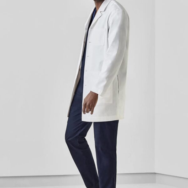 Man in a white lab coat and navy scrubs, standing and smiling.
