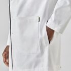 Person in a white lab coat with hand in pocket against a neutral background.