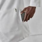 Person in a white coat putting a smartphone into their pocket.