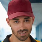 Man wearing a maroon baseball cap, smiling, and standing indoors.