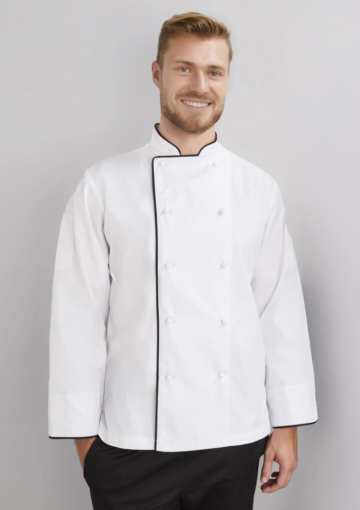 Smiling man in a white chefs jacket stands against a light gray background.