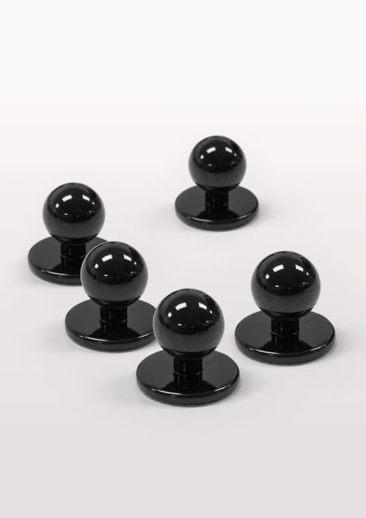 Five black magnet pieces with rounded tops on a white surface.