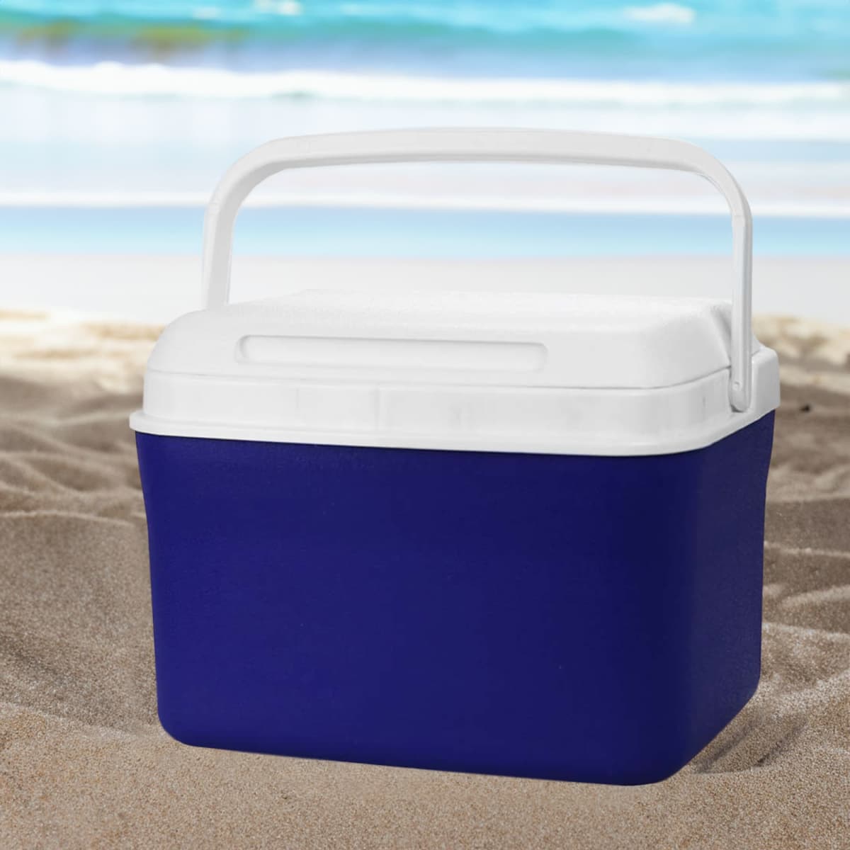 Blue and white cooler on sandy beach with ocean waves in the background.