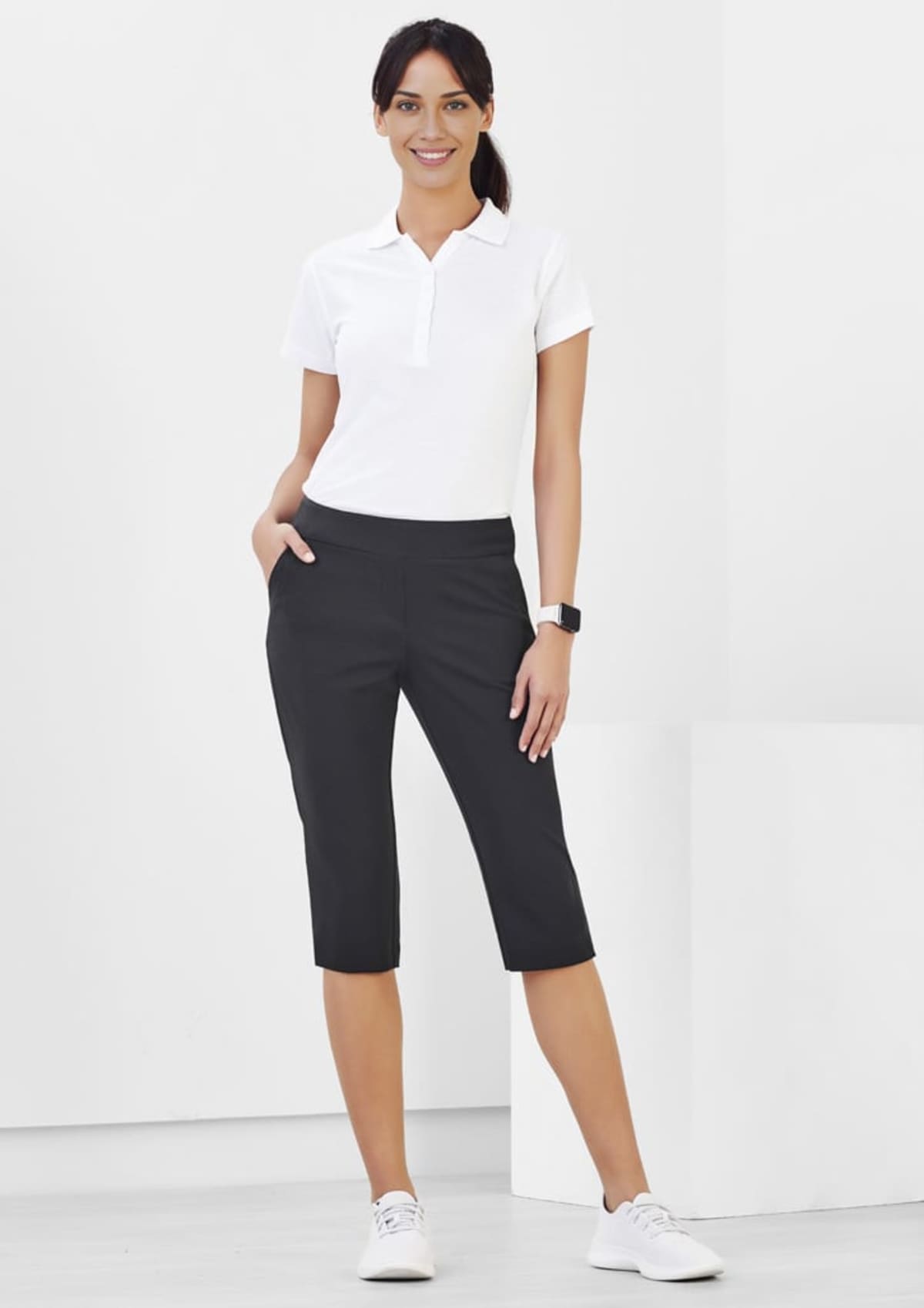 Person wearing white polo, black pants, and white sneakers poses with hands in pockets.