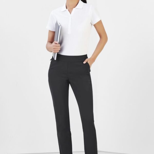 Person in a white polo and black pants holding a notebook, standing in a minimalistic room.