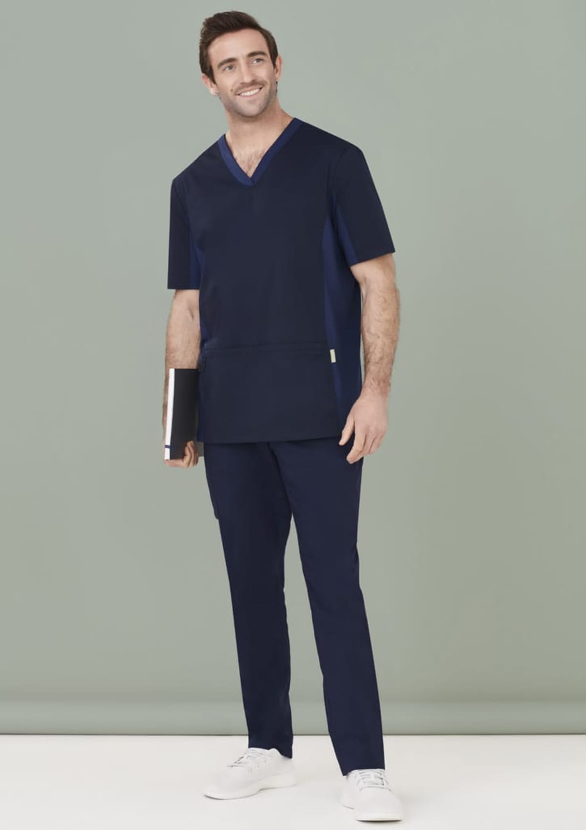 Person in navy blue scrubs holding a notebook, smiling against a light green background.