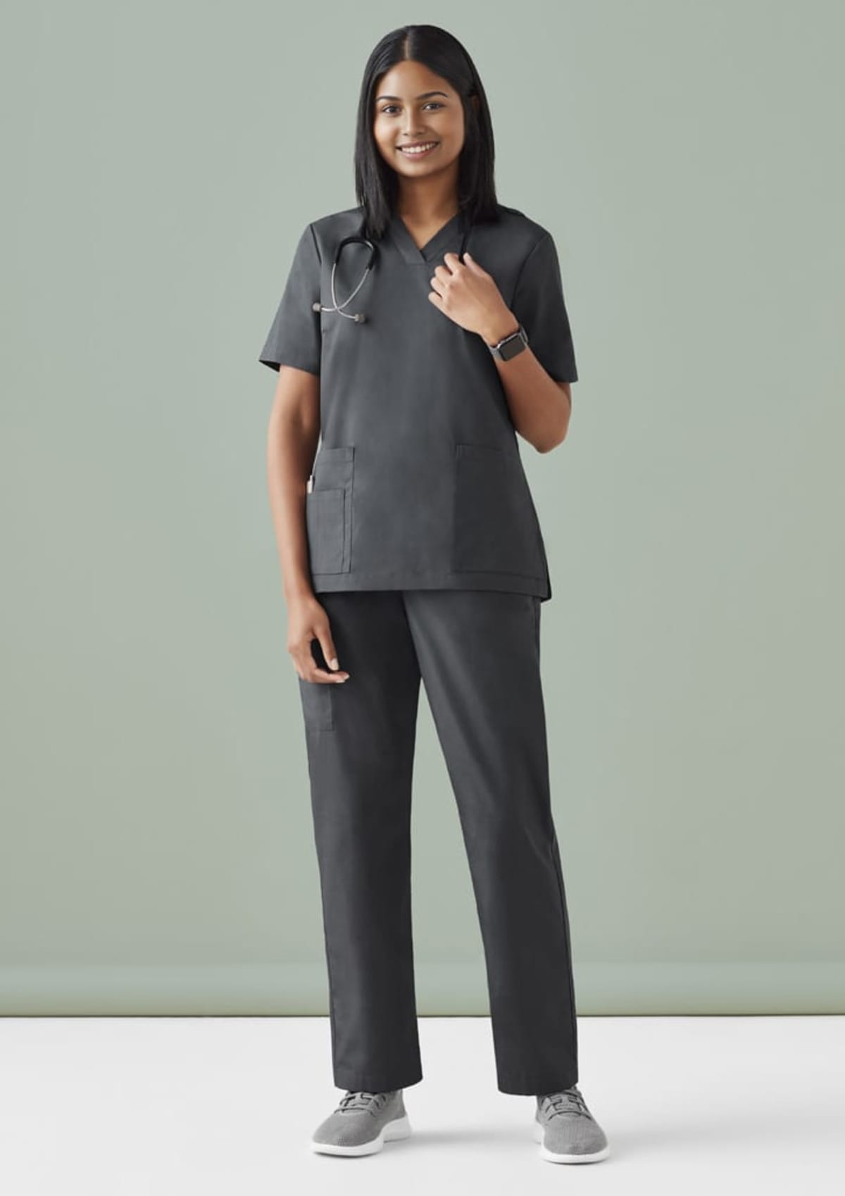 Person in gray scrubs with a stethoscope against a light green background.