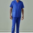 Person in blue medical scrubs and white sneakers stands against a plain backdrop.
