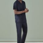Person wearing a navy scrub outfit stands against a light green background.