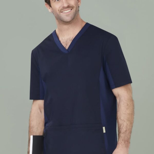 Man in navy scrubs holding a notebook and smiling against a gray background.