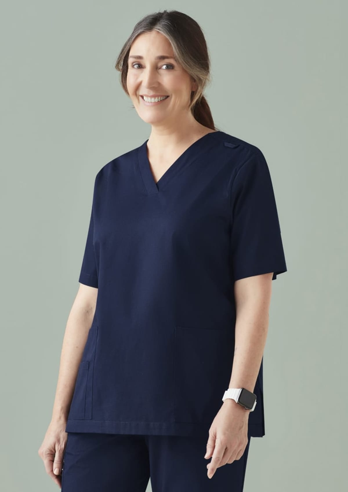 Smiling woman in dark blue medical scrubs, standing against a plain background.