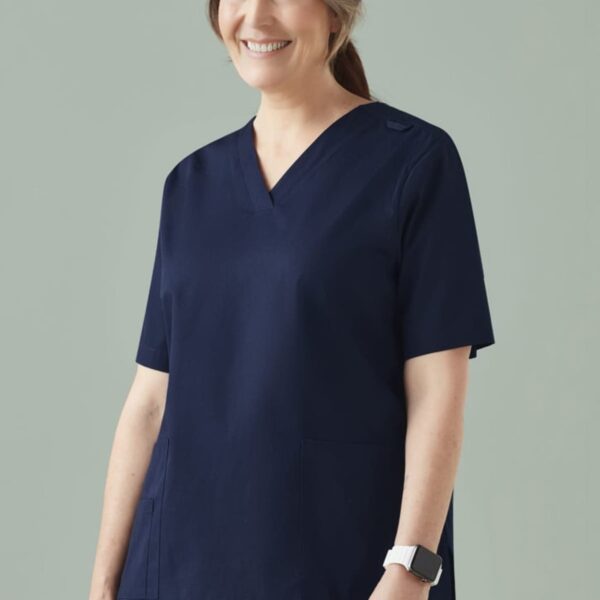 Smiling woman in dark blue medical scrubs against a plain background.