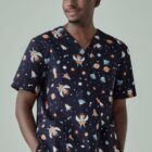 Smiling person wearing space-themed scrubs with rockets and astronauts.