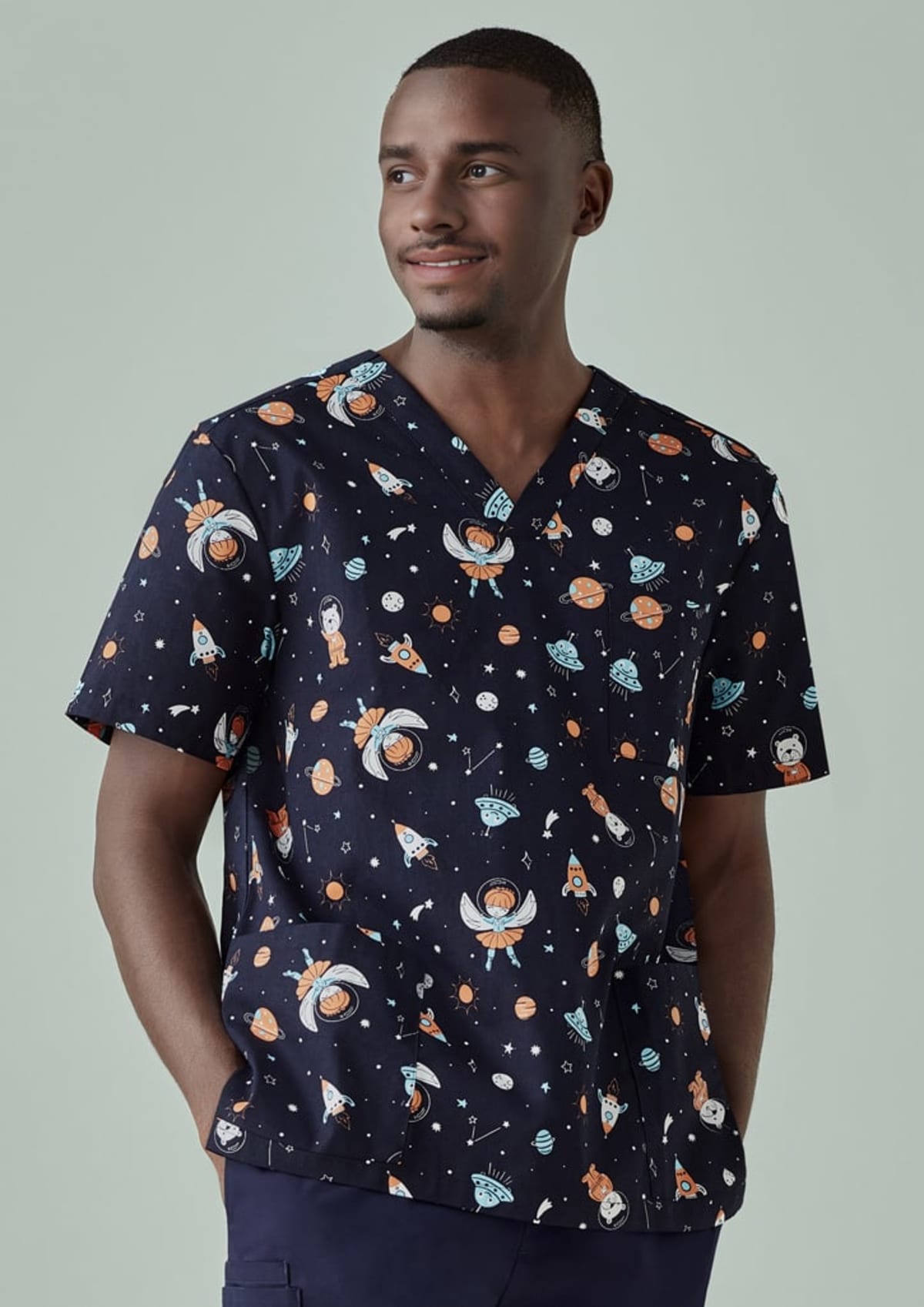 Smiling person wearing space-themed scrubs with rockets and astronauts.