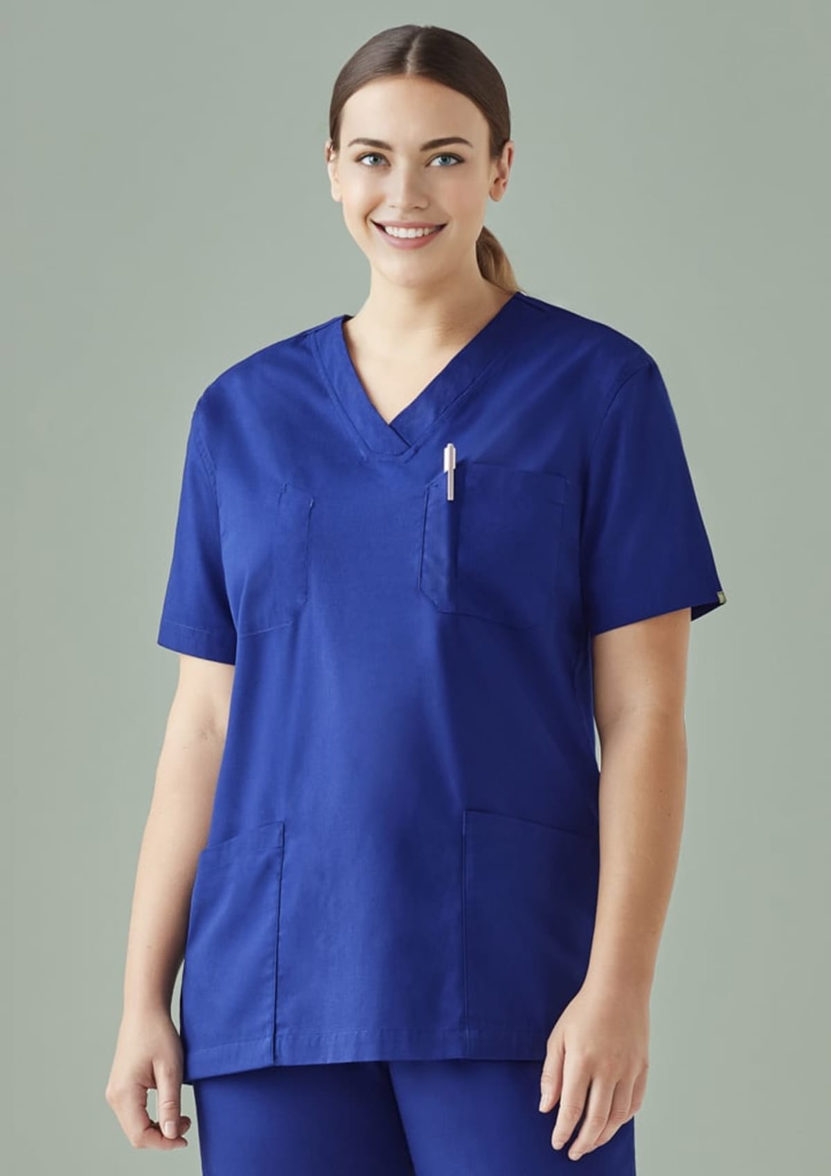 Person in blue scrubs smiles against a light green background.