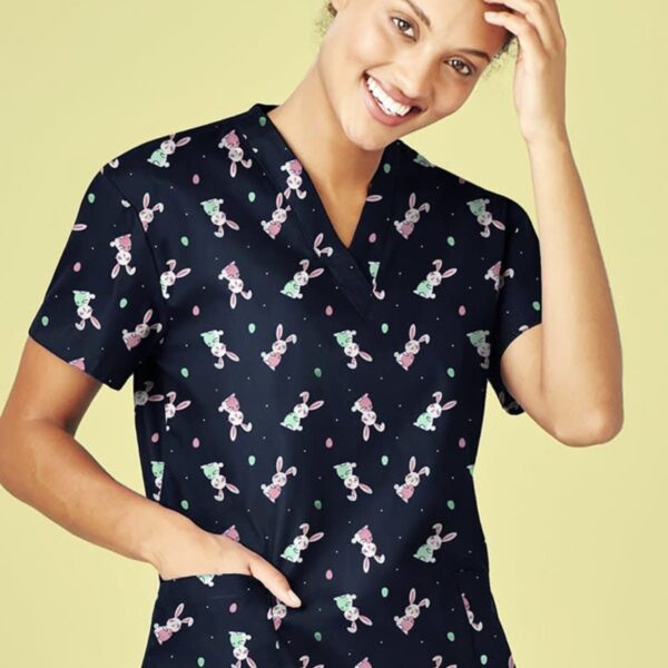 Person in a teddy bear patterned scrub top, smiling with one hand on head.