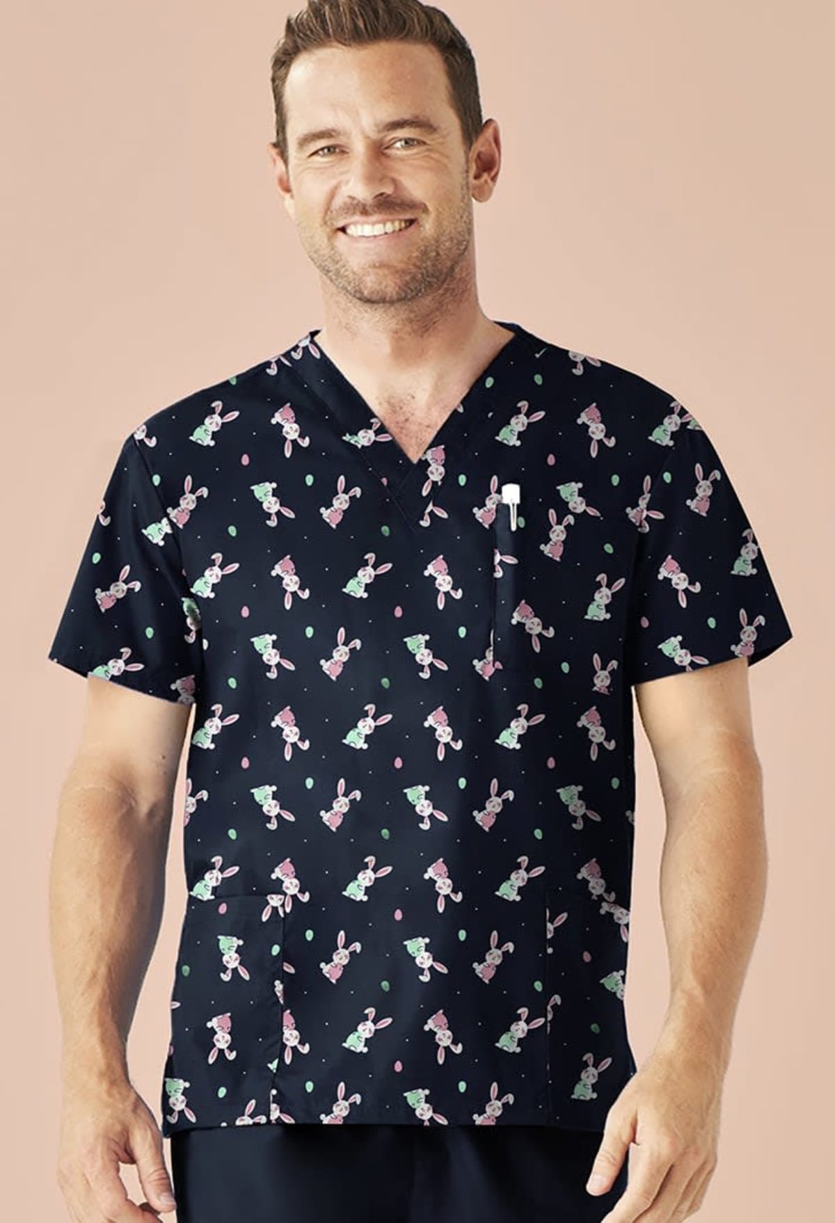 Man in dark scrub top with colorful rabbit pattern, smiling against a beige background.