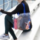 Person seated with a clear tote bag containing various items on bleachers by a track.