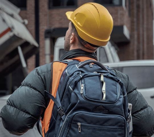Person in a hard hat with a backpack, highlighting workplace safety at a construction site.