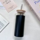 Black tumbler with a wooden lid and metal straw on a white surface.