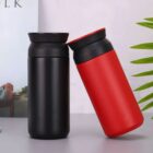 Two insulated tumblers, one black and one red, leaning against each other on a table.